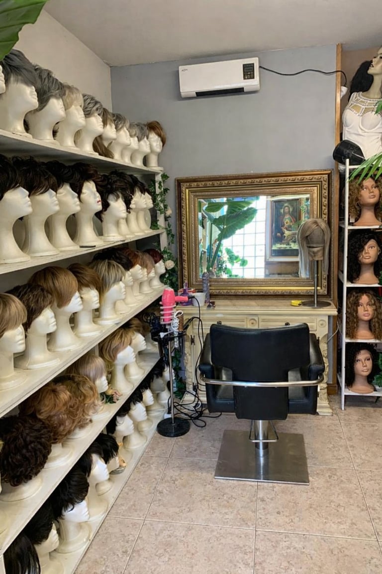 Beauty supply shop interior with mannequin heads wearing wigs on shelves, a mirror, styling chair, and hair display on right wall